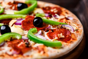 Pizza with chorizo ​​sausage, mozzarella cheese, green pepper and black olives. Rustic wooden background. Soft focus.	