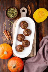 Autumn pumpkin cupcakes or baked muffins with fresh pumpkin and pumpkin seeds for Thanksgiving day on dark wooden background. Top view, vertical photo