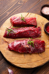 Raw beef steak. Raw fresh farm steak with rosemary, salt and pepper on cutting board on wooden background. Raw beef steak and spices for cooking