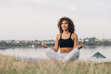 Young woman practicing yoga near the river at sunset