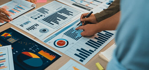 A group of professionals collaborates over various business charts and graphs, engaging in lively discussion and strategic planning for future projects and performance evaluation. SACTR