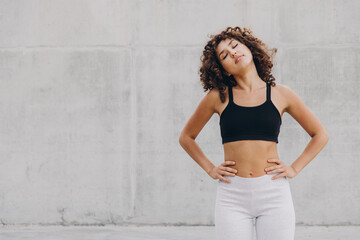 Young sportswoman stretching neck against concrete wall
