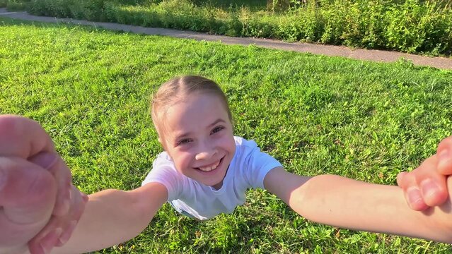 Girl kid holds her dad hand, daughter dad are spinning together on lawn. Daddy baby girl playing on grass in park holding hands. Happy family. Father kid daughter are having fun together in meadow POV - Powered by Adobe