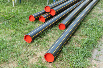 stack of black pipes with red caps is ready for installation on a grass. tubes components for a new gas supply infrastructure network.