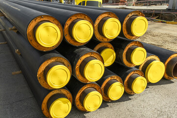 Stacked insulated tubes with yellow protective caps are placed at a construction site. water pipes are for utility installation