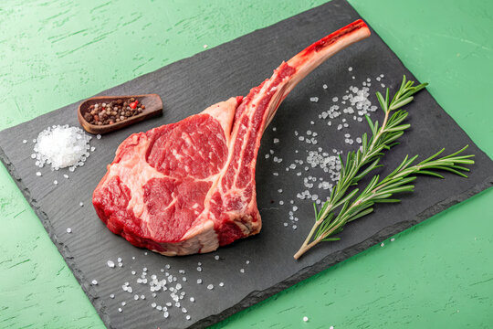 Fresh Tomahawk Steak on Slate Board with Green Background