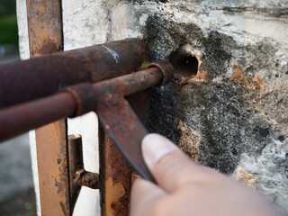 Hand interacts with rusty metal gate latch against weathered concrete wall