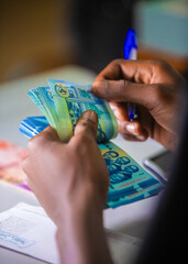 Dark skinned African person working on desk holding counting Ghanaian cedi notes in hand. accounting concept