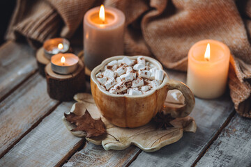 Spicy sweet fall hot drink: delicious pumpkin latte with cinnamon, marshmallow with salted caramel. Served in handmade artisan mug in shape of pumpkins, cozy home decor with candles, dry autumn leaves
