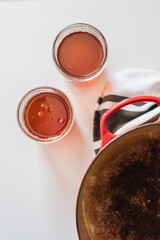 Homemade ghee process in bright natural light, golden clarified butter in glass mason jars beside a red cast iron pot and striped tea towel, high contrast kitchen scene with warm shadows and bright