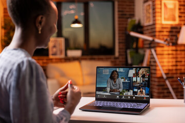 Busy woman sitting at desk in home office during sunset, attending virtual conference with colleagues on digital device. Financial consultant presenting strategies to company employees on video call.