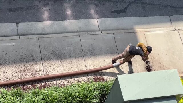 Man sprays mulch along a sidewalk viewed from above