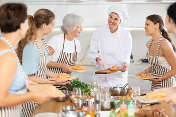 Girl chef tells group of students listeners of cooking courses about secrets of cooking juicy and tender chicken fillet.