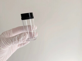 A gloved hand holding a small transparent sample Test tube against a plain light background