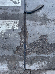 Close-up view of a damaged road surface with cracks and exposed asphalt lines.