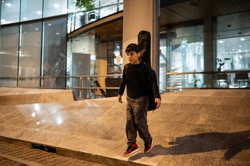 Young musician walking with guitar case in city at night