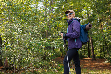 Smiling hiker with backpack and trekking poles in summer forest