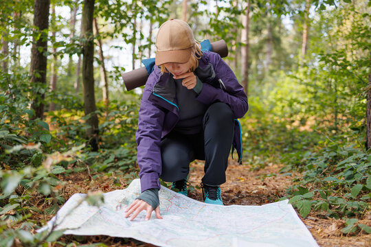 Female traveler kneeling on forest path and studying paper map