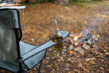 Beer bottle in chair pocket near campfire on forest campsite