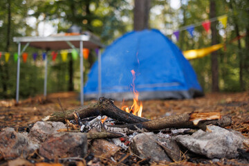 Campfire burning near tent and camping table in forest campsite