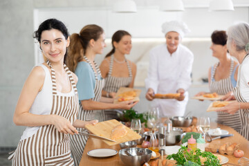 Young woman in apron learns to cook chicken dish at cooking master class