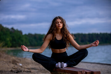 A woman meditates peacefully by a serene lake at sunset, enjoying natures calm