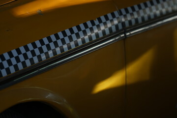 Detail shot of a vintage yellow taxi car showing black and white checker stripe pattern on the door. Classic retro cab design with sunlight and shadows creating nostalgic atmosphere