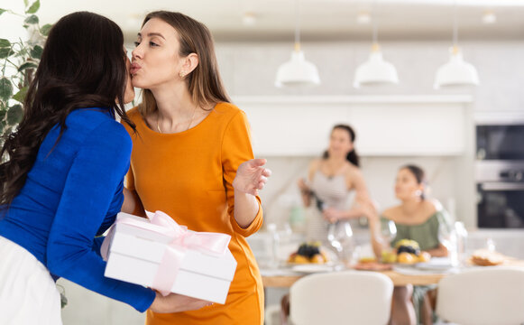 Woman joyfully greets her friends on the doorstep, hugging and kissing each other