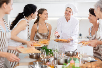 Young female chef at master class teaches group of people how to cook chicken