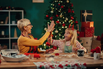 Grandmother and granddaughter giving high five while baking christmas cookies
