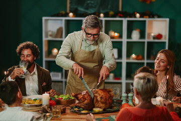 Grandfather carving thanksgiving turkey for family dinner