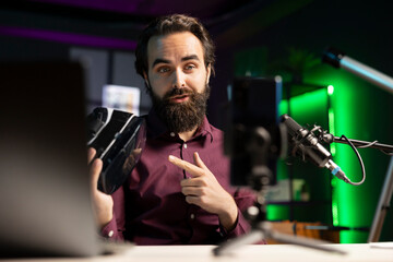 Tech specialist reviewing futuristic VR goggles in studio using smartphone on tripod. Media star filming technology channel vlog using mobile phone, showcasing virtual reality glasses