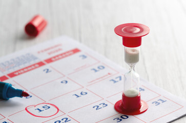 An hourglass with white sand on a calendar and a red marker. 