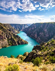 Fototapeta premium A breathtaking view of a turquoise river winding through a dramatic canyon, showcasing rugged mountains and lush vegetation under a vibrant sky.