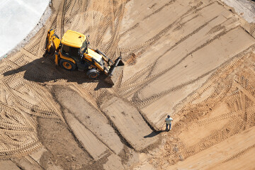 Yellow excavator and construction worker on building site preparing ground
