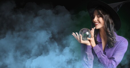 Young witch with crystal ball on dark background with space for text