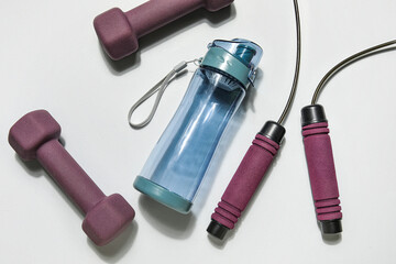 Sports water bottle, jumping rope and dumbbells on white background