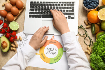 Female nutritionist typing with laptop near fruits and vegetables on table