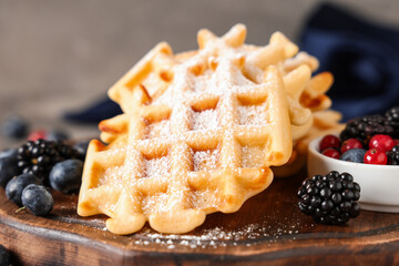 Delicious Belgian waffles with berries on board on table against grey background. Closeup