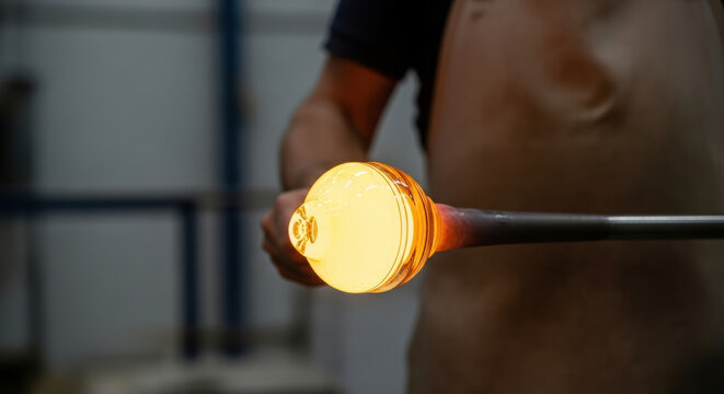 Skilled artisan forming molten glass with blowpipe in workshop, focused craftsman shaping glowing orb, traditional manual glassblowing process, craftsmanship and creativity