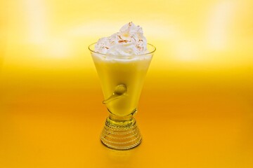 A fancy glass of eggnog with whipped cream and cinnamon on top. The backround a metallic gold.