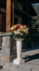 Vibrant flower arrangement in a classic white urn sits on a stone porch of a rustic building, bathed in sunlight