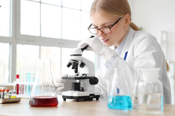 Fototapeta premium Female scientist looking through microscope in laboratory