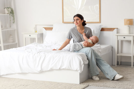 Young mother suffering from postnatal depression with her baby in bedroom