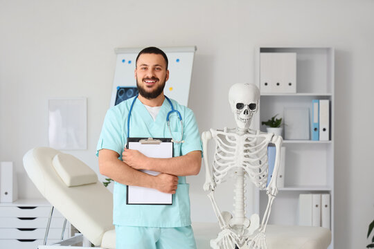 Male doctor with clipboard and human skeleton in clinic