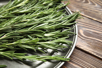 Plate with fresh rosemary twigs on wooden background, closeup