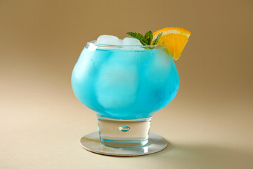 Glass of tasty Blue Lagoon cocktail garnished with orange and mint on beige background