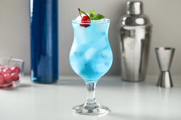 Glass of tasty Blue Lagoon cocktail garnished with cherry and mint on white table