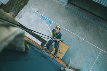 
Firefighter rescuer descending a massive wall using a rappelling device in a multi-story building, wearing protective gear such as a helmet, harness, and carabiners.