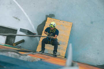 
Firefighter rescuer descending a massive wall using a rappelling device in a multi-story building, wearing protective gear such as a helmet, harness, and carabiners.